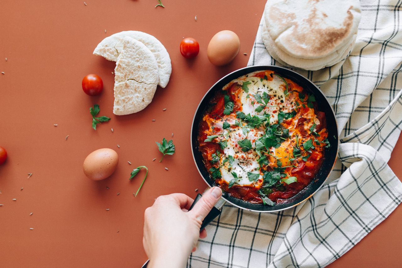 A vibrant shakshuka dish with pita, eggs, and fresh ingredients on a rustic backdrop.